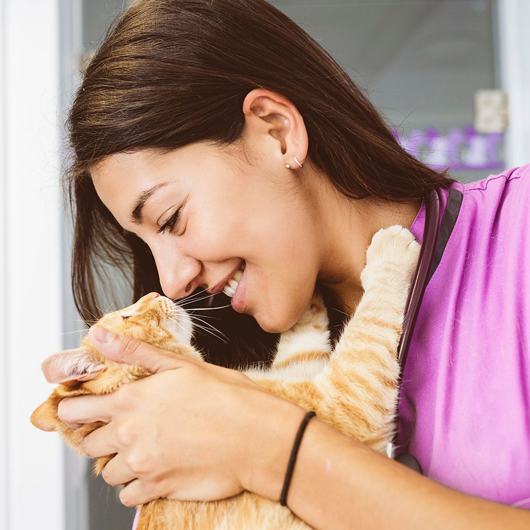 female veterinarian smiling while cuddling and holding orange striped tabby cat